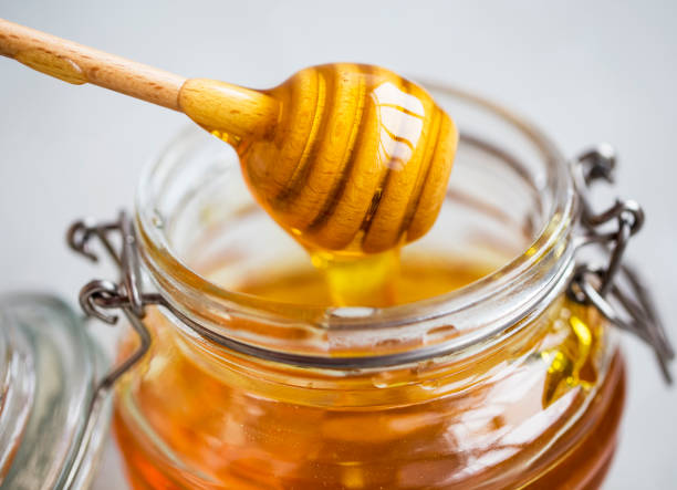 rohe bio-honig in einem glas mit dipper closeup, gesundes natürliches süßungsmittel - syrup jar sticky isolated objects stock-fotos und bilder