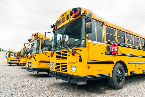 Horizontal shot of a line of parked yellow school buses under a cloudy sky.