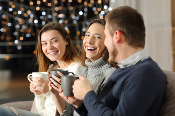 Three friends talking and laughing in the night at home Three friends talking and laughing in the night sitting on a couch in the living room at home family christmas party stock pictures, royalty-free photos & images