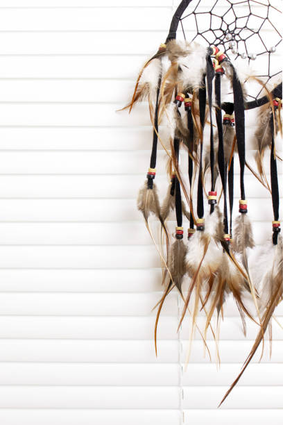istock Dream catcher with feathers threads and beads rope hanging, white window blinds on background. Dreamcatcher handmade. 1044355276