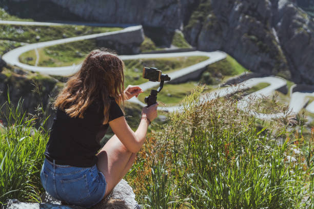 young woman filming the tremola road in san gotthard using a smartphone and a gimbal girl using an image stabilizer with his phone in the swiss alps lepontine alps stock pictures, royalty-free photos & images