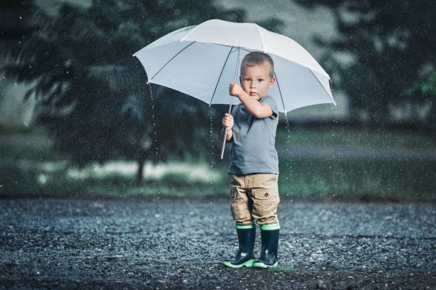 istock Adorable child holding an umbrella in a rain storm 1044358424