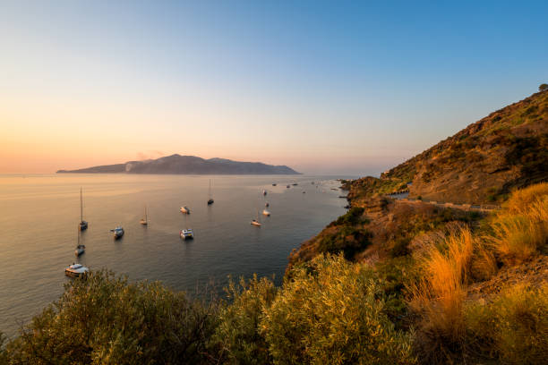 Sicily, Italy - August 16, 2017: Sicily  view showing Aeolian island, mountains with houses, trees, boats and ferries in the sea with sunset