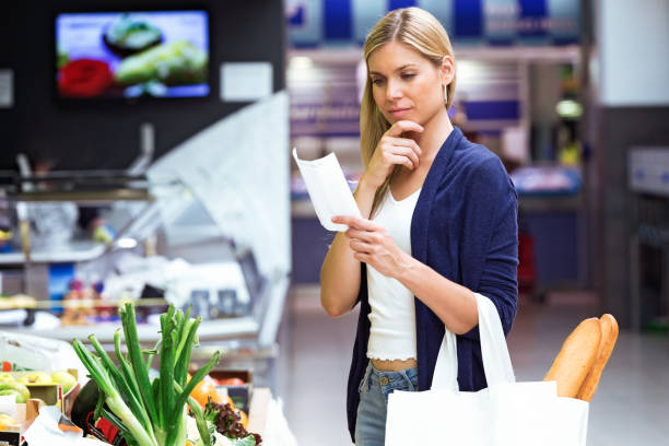 beautiful young woman buying fresh vegetables and looking shopping list in the market. - tomato women green market imagens e fotografias de stock