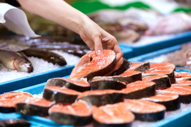 jovem vendedor escolhendo uma paz de salmão no mercado. - variation catch of fish fish prepared fish - fotografias e filmes do acervo