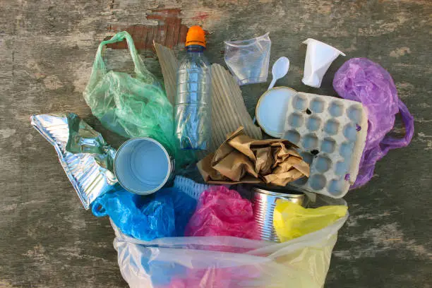 Photo of Garbage bag with different trash on wooden background. Top view. Flat lay.