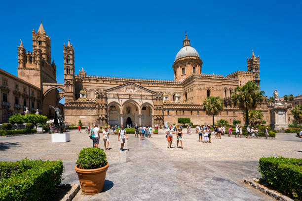 Palermo, Sicily, Italy - August 7, 2017: Palermo  view showing Santa Maria Assunta Cathedral with trees, grass, statue , people walking and taking pictures can be seen on the background