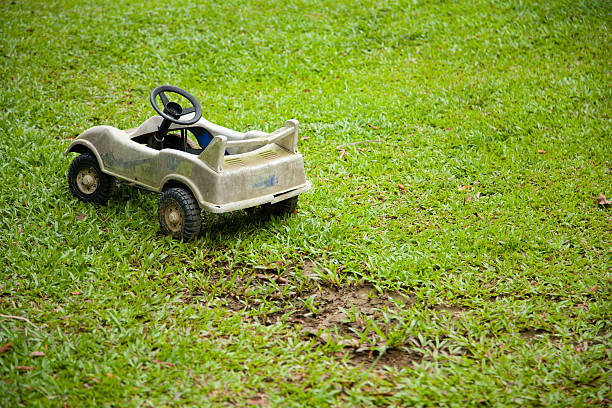 A peasant boy plays outdoors in a rural Andean landscape, dragging a toy vehicle over wet grass, while a dense fog covers the horizon. The image reflects rural childhood, creativity with simple resources and connection with nature.