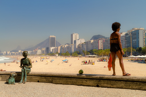 Rio de Janeiro, Brazil - August 20, 2018: Young African-American woman looks at the beach of Leme next to the statue of the writer Clarice Lispector