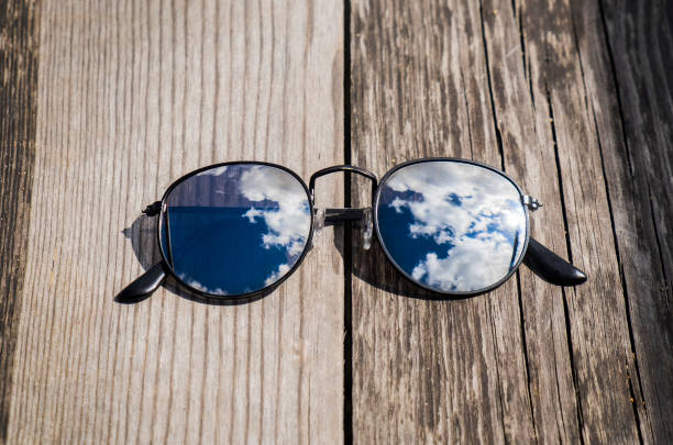 istock Mirrored sunglasses close up on the wooden pier with clouds and sky reflection 1044409084