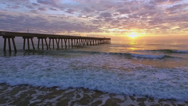 DRONE. Low level aerial view of Johnny Mercer's Pier and waves crashing on shore during epic sunrise