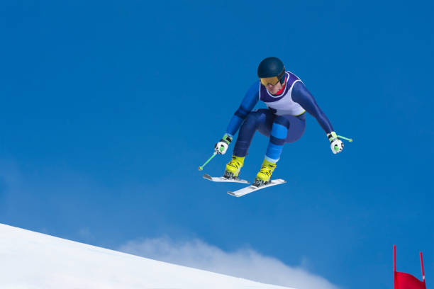 Front view of young male skier jumping during the downhill ski race against the blue sky