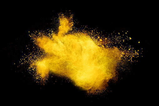 Abstract brown powder explosion. Closeup of yellow dust particle splash isolated on black background