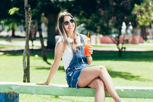 Portrait of a beautiful young woman, drinking juice on a sunny day in the park
