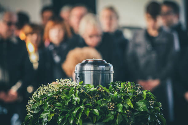 Metal urn at a funeral A metal urn with ashes of a dead person on a funeral, with people mourning in the background on a memorial service. Sad grieving moment at the end of a life. Last farewell to a person in an urn. place of burial stock pictures, royalty-free photos & images