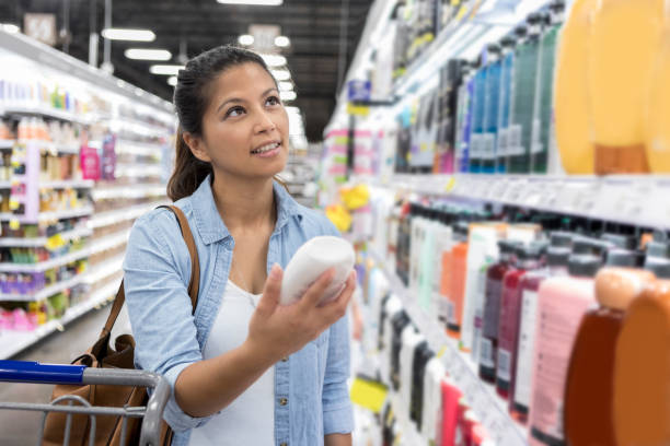 Woman shops for shampoo in supermarket Confident mid adult woman browses a large selection of shampoo while shopping in grocery store. She is holding a bottle while checking out the price. shampoo stock pictures, royalty-free photos & images