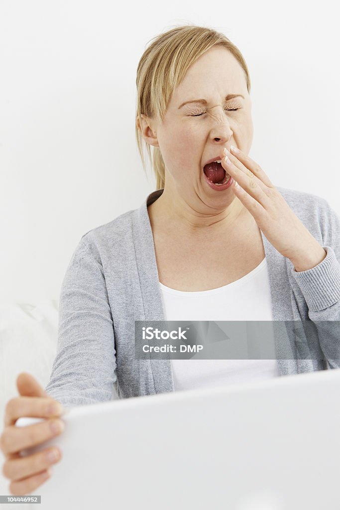 Bela jovem mulher bocejando com um laptop em seu colo - Foto de stock de Bocejar royalty-free