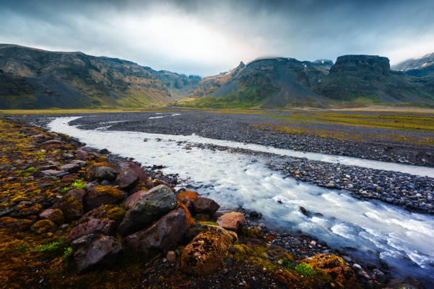 Typical Iceland landscape with river and mountains. Dramatic sky and red stones on a foreground