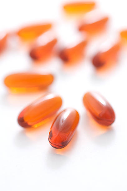 gel ambre capsules sur blanc - vitamin pill vertical high key photographic effects photos et images de collection