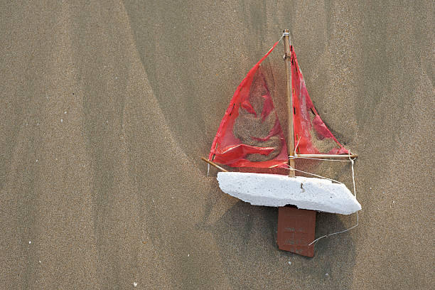 View from above of a home made sail boat complete with mast, keel, hull and sail is washed up on sand in late afternoon sun