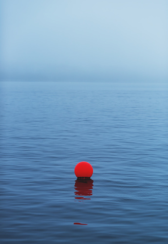 A single buoy floating in a fog shrouded harbour.