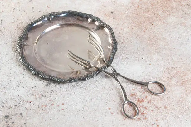 Vintage silverplate dish and serving tongs on concrete background. Copy space for text.