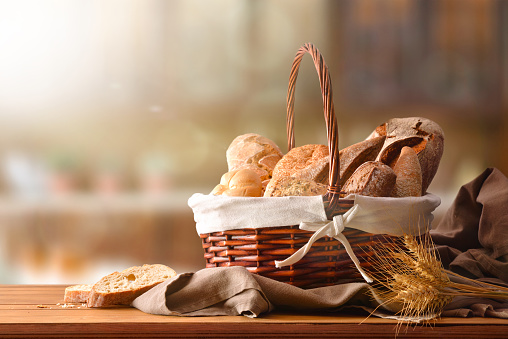 Assortment of breads over a wicker basket on a cloth over a table in a rustic kitchen. Horizontal composition. Front view