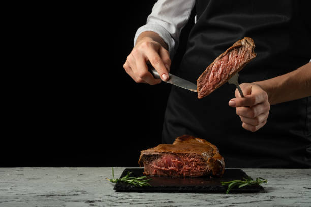 istock Chef, cut with a meat steak on a black background with an open space for text or restaurant menus. Horizontal photo Black text area. 1044492934