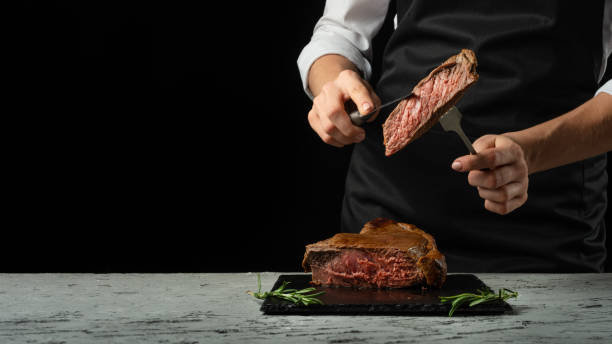 istock Chef, cut with a meat steak on a black background with an open space for text or restaurant menus. Horizontal photo Black text area. 1044495348