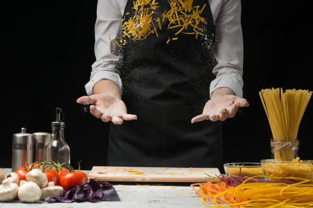 Cooking macaroni spaghetti dough with flour on a dark black background with vegetables. concept preparation of spaghetti, pasta, Italian pasta, large size solution.
