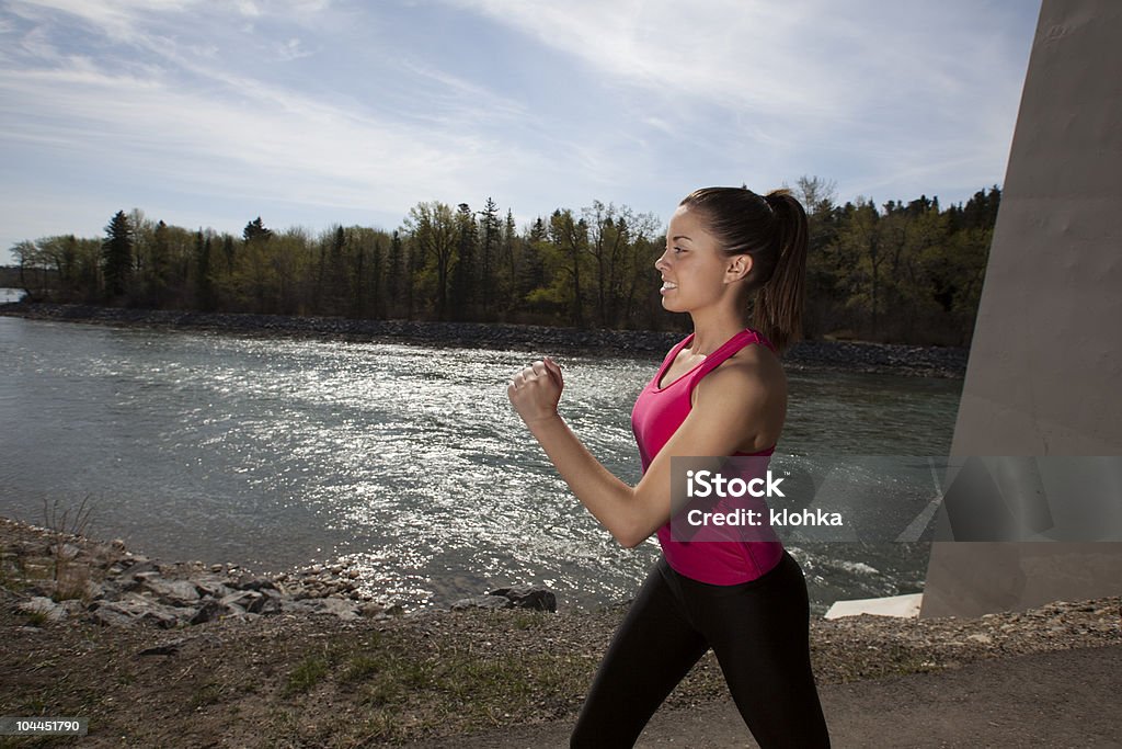 Young Woman Power Walking Young woman power walking near river with sunlight reflecting on the water. Active Lifestyle Stock Photo