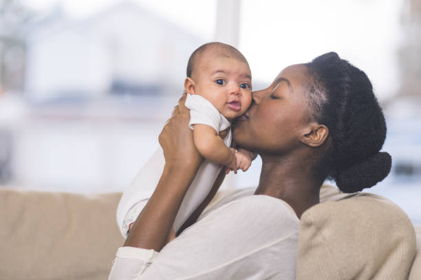 美しいアフリカ系アメリカ人の母が居間で生まれたばかりの赤ちゃんを保持します。 - baby mother newborn african descent ストックフォトと画像