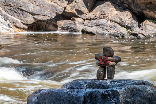 An inukshuk with a natural red maple leaf on it's front, stands on a large rock overlooking the York River, as it rushes over the Egan Chute near Bancroft, Ontario, Canada.
