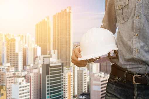 Engineering man standing with white safety helmet with building construction site against background