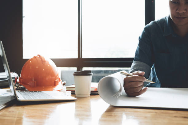 istock architect drawing on blueprint architectural, Young man working on his plane project at site construction work - Engineering construction  Concept 1044634174