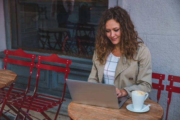 istock smiling woman working at laptop in outdoors cafe 1044639906