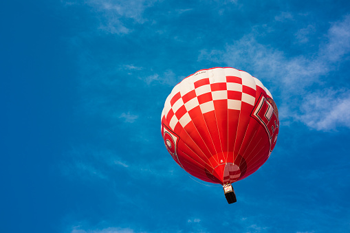 isolated gas filled red and white observation balloon. tourist attraction. round passenger basket. blue sky background with white clouds. leisure and outdoors