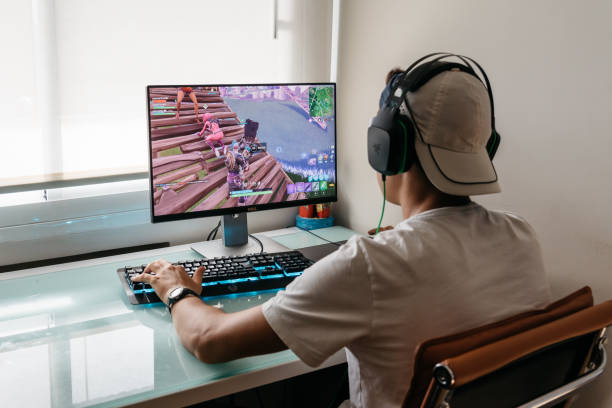 Teenager playing Fortnite video game on PC Madrid, Spain - August 15, 2018: Teenager playing Fortnite video game on PC. Fortnite is an online multiplayer video game developed by Epic Games only teenage boys stock pictures, royalty-free photos & images