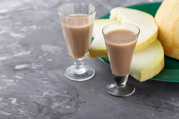 Homemade milk liqueur in two glasses with melon, on concrete table. Copy space