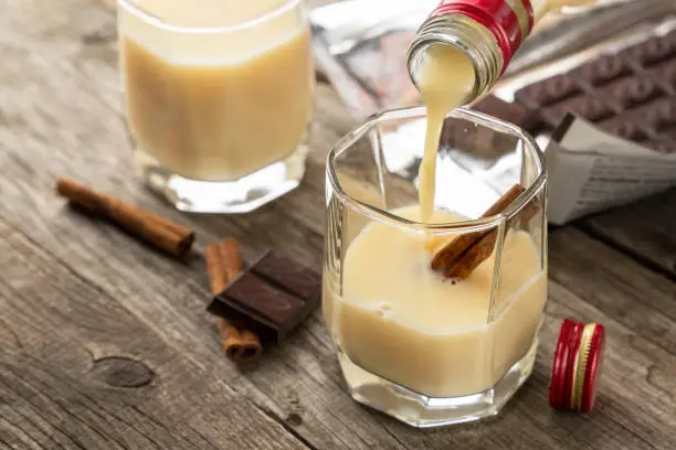 Milk liqueur in two glasses with cinnamon and chocolate, on a wooden table