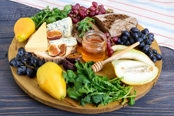 istock Assortment of appetizer: grapes, cheese, blue cheese, figs, melon, arugula, grain bread, honey on a round wooden tray on a wooden table 1044672336