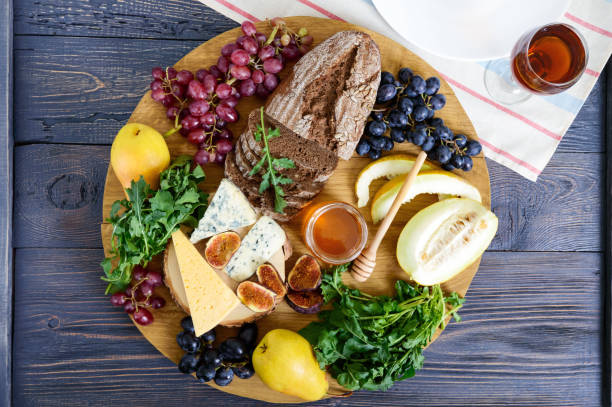 istock Assortment of appetizer: grapes, cheese, blue cheese, figs, melon, arugula, grain bread, honey on a round wooden tray on a wooden table Top view. 1044672342