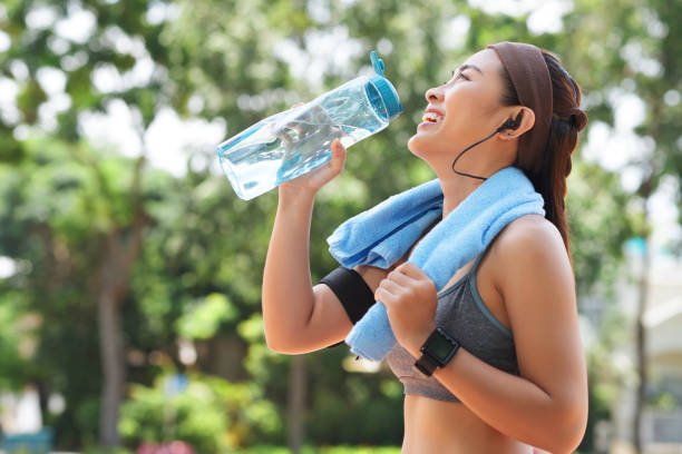 幸せなスポーツウーマンの公園で水を飲む - arm band ストックフォトと画像