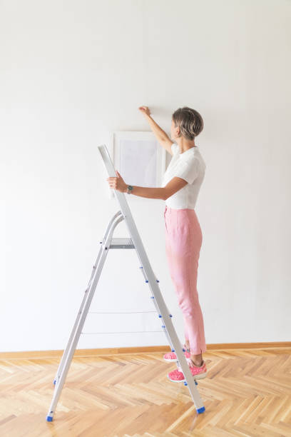 istock Woman hanging painting using ladder 1044692654