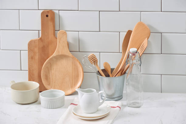 istock Simple rustic kitchenware against white wooden wall: rough ceramic pot with wooden cooking utensil set, stacks of ceramic bowls, jug and wooden trays. 1044707890