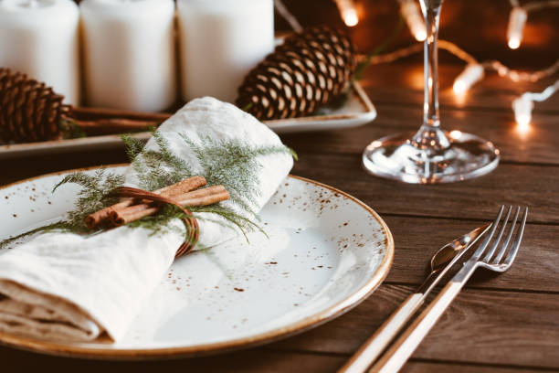 thanksgiving table setting among white candles and cones. ceramic plate with fork and knife on a linen napkin. the concept of a festive dinner. - christmas table imagens e fotografias de stock