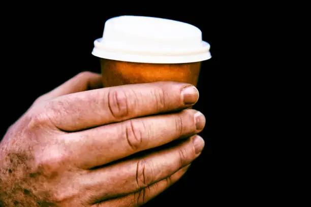High contrast image of a small coffee cup in an older man’s hand.
