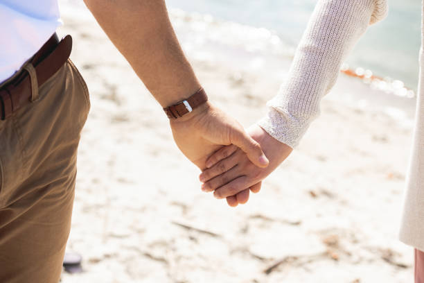istock partial view of couple holding hands while walking on sandy beach 1044715124