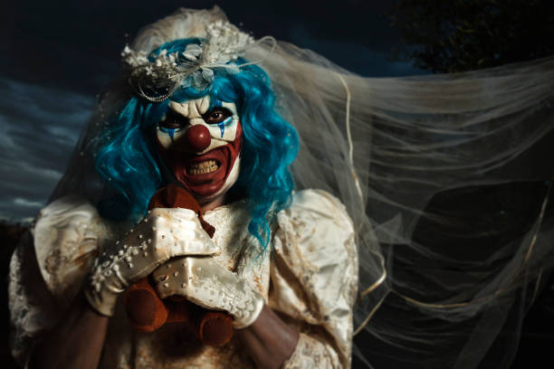 evil clown in bride dress strangling a teddy bear closeup of a scary evil clown wearing a dirty and ragged bride dress, strangling a teddy bear, in a disturbing rural landscape at dusk scary bride stock pictures, royalty-free photos & images