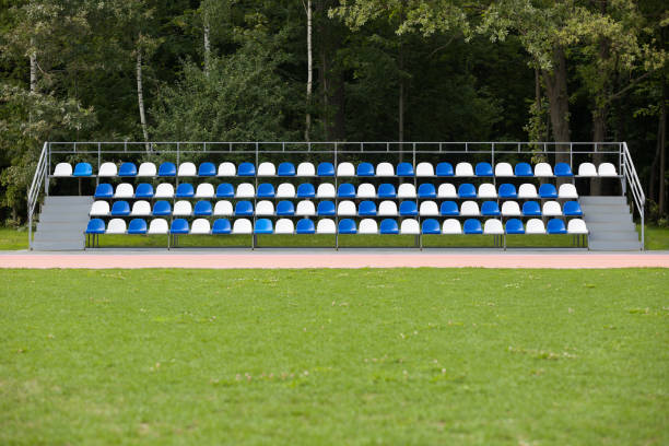 sedili vuoti blu e bianchi in un footbal o in uno stadio di calcio. campo in erba e sedie in plastica, arena sportiva a porte aperte. - bleachers stadium seat empty foto e immagini stock